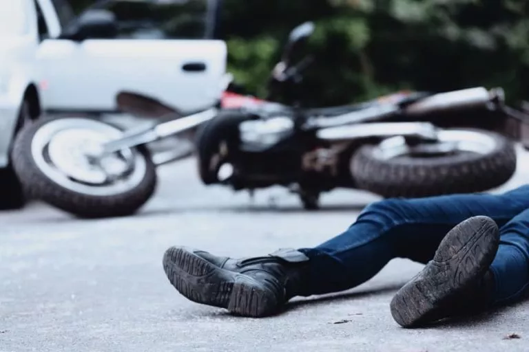 A man lying on the road after a motorcycle accident with crashed bike and car in the background
