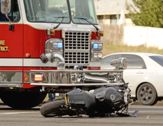 A wrecked motorcycle on the ground in front of a large red fire truck.