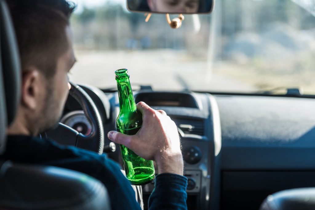 Close-up of a man driving with a beer in his hand and blurred road and vehicles in front of him