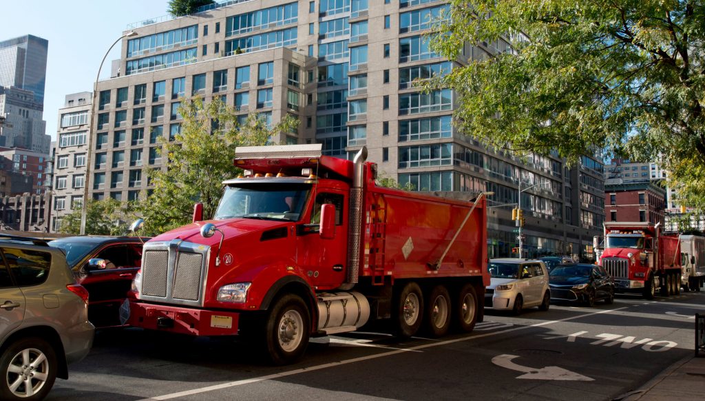 Large red dump truck in traffic on a road in Manhattan, NYC