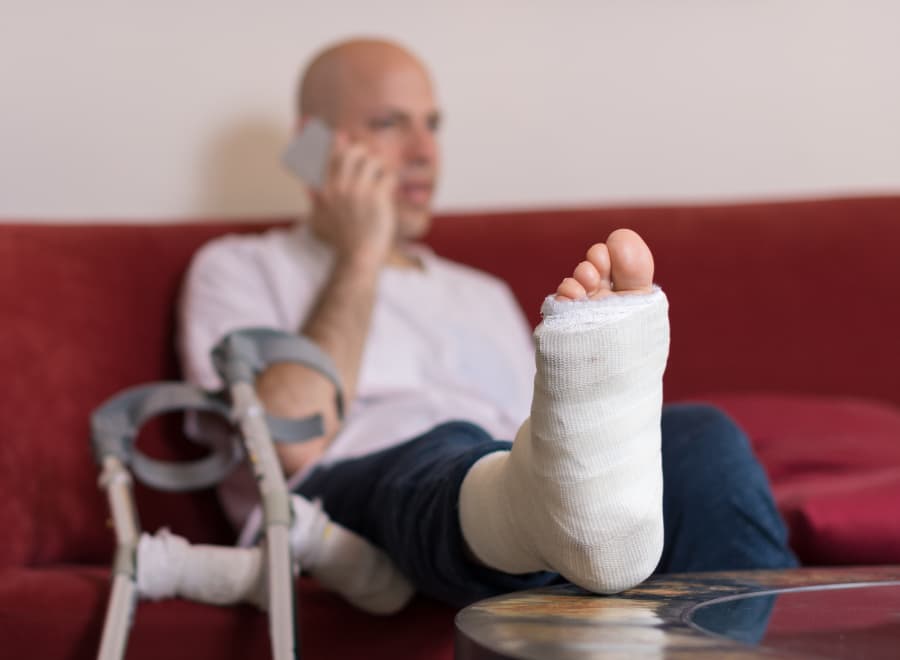 Blurred image of a man with his leg in a cast speaking on the phone.